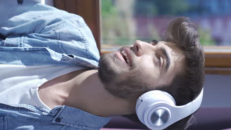 Vertical-video-of-Man-looking-out-the-window-and-listening-to-music-with-headphones.